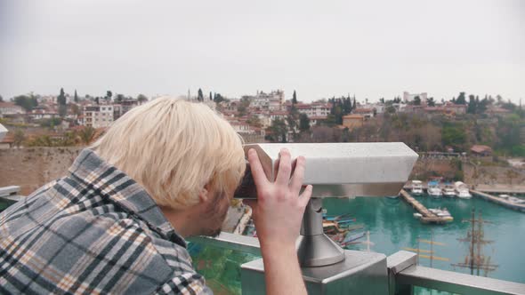 Blonde Man in a Plaid Shirt Looking at Sea Port Through the Telescope From the Observation Deck