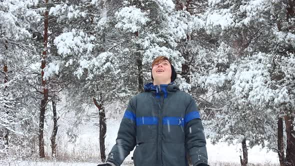 a Young Teenager Man of European Appearance in Warm Winter Clothes Stands in a Snowy Forest and