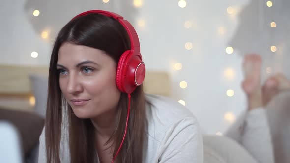 A Beautiful Girl is Lying on the Bed Using a Mobile Computer and Listening to Music on Headphones