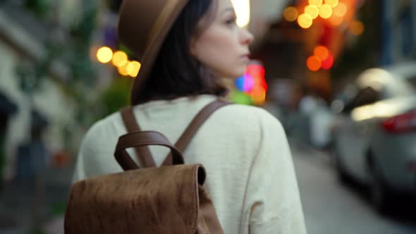 Portrait of a young woman in a hat looking back on the street on a trip