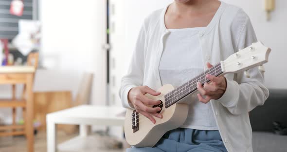 Woman play song on ukulele at home