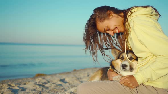 Candid Laughing Latin Girl in Yellow Hoodie at Summer Beach with Cute Pet Corgi Dog Sitting in Front