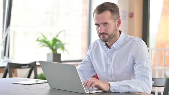 Cheerful Young Man with Laptop Pointing with Finger