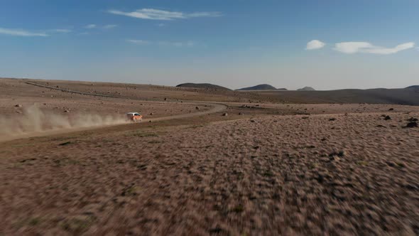 Aerial View Drone Following a Car Stirring Up a Large Dust Cloud As It Speeds Along Desert Road