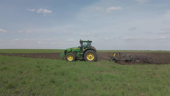 A rural tractor drags a plow across a field with rising dust