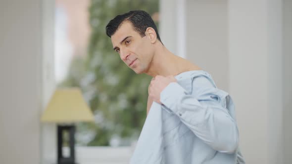 Middle Shot Portrait of Muscular Tattooed Man Putting on Shirt Indoors