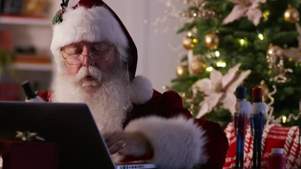 Santa Claus in workshop using laptop computer alt
