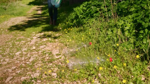 a Female Volunteer with a Plastic Bag of Garbage Walks Along the Road Near the Forest and Collects