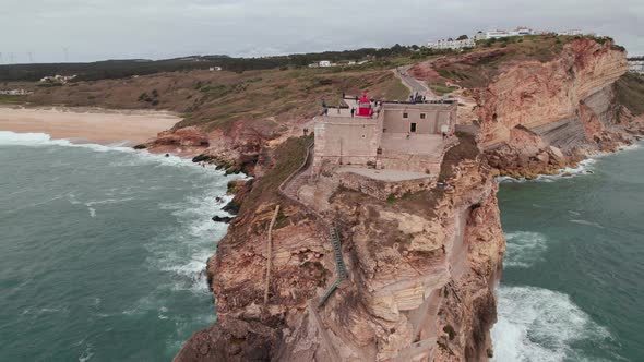 Aerial View of a Lighthouse on a Cliff with a Fortress in Nazare Town Portugal