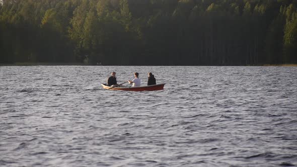 Young adults racing and rowing a boat on a lake at sunset.