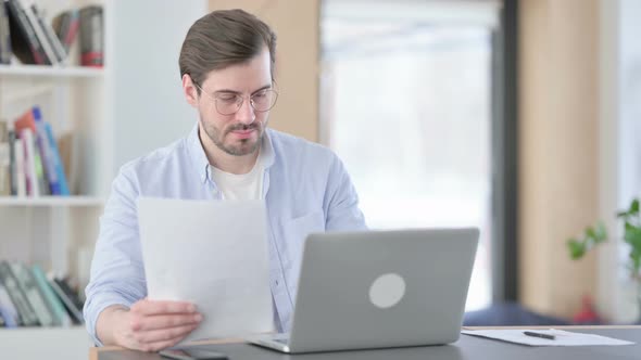 Young Man with Laptop Reading Documents