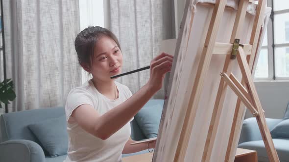 Asian Artist Girl Sitting And Holding Paintbrush Painting On The Canvas