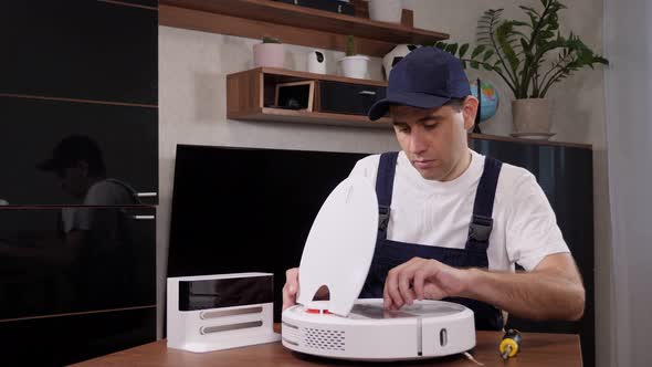 A Male Handyman Repairs a Robotic Vacuum Cleaner While Sitting at a Table