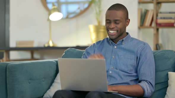 Online Video Call on Laptop By Young African Man on Sofa 