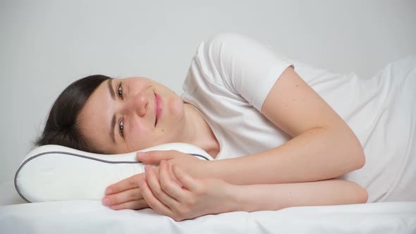 A Woman Lies on an Orthopedic Pillow Made of Memory Foam and Smiles Looking Into the Camera
