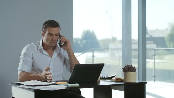 Business Man Working at Laptop Computer. Concentrated Man Talking Mobile Phone