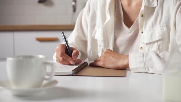 A Young Housewife Drinks Coffee In The Kitchen Writing Down Her Dreams And Goals In A Diary