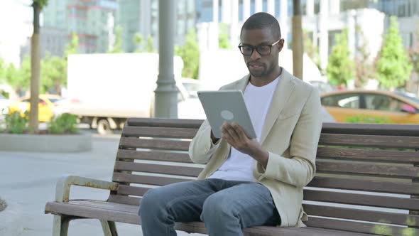 African Man Using Tablet While Sitting Outdoor on Bench