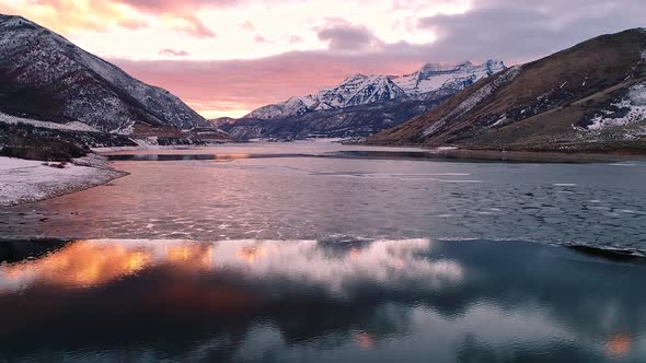 Flying toward colorful sunset over partial frozen lake in Utah