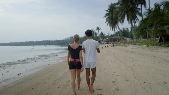 Back View of Interracial Couple Walking on an Exotic Island Beach at Sunset