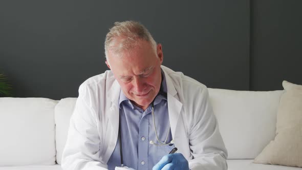 Caucasian senior male doctor taking notes and waving while having a video call