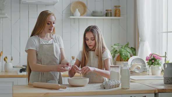 Caring Mother Woman Blonde with Long Hair Teaches Little Daughter Girl Child Cook Kid Breaks Eggs