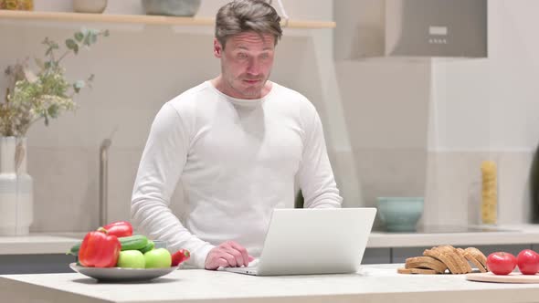 Middle Aged Man Doing Video Call on Laptop in Kitchen