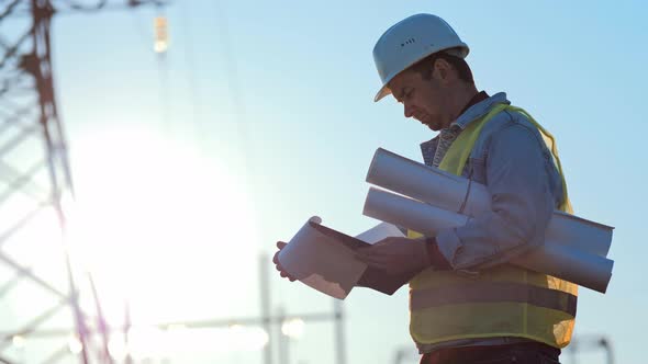 Foreman Stands on Construction Site and Holds Drawings on Paper in Hands