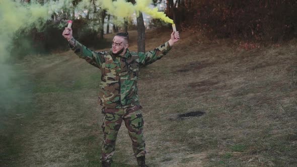 Soldier in a Camouflage Uniform and Walks in Nature with Colored Smoke