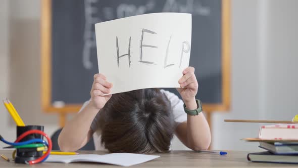 Exhausted Cute Schoolboy Putting Head on Desk and Raising Help Written on Paper