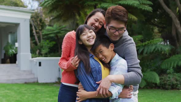 Smiling asian parents hugging happy son and daughter in garden