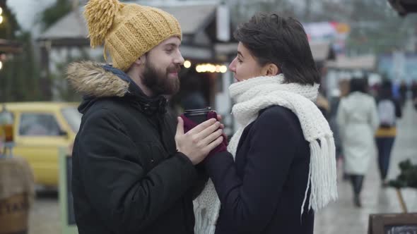 Side View of Man and Woman in Love Standing at Winter Fair and Looking at Each Other. Bearded