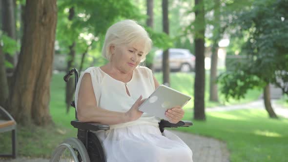 Positive Handicapped Senior Woman Messaging Online Outdoors. Portrait of Beautiful Paralyzed