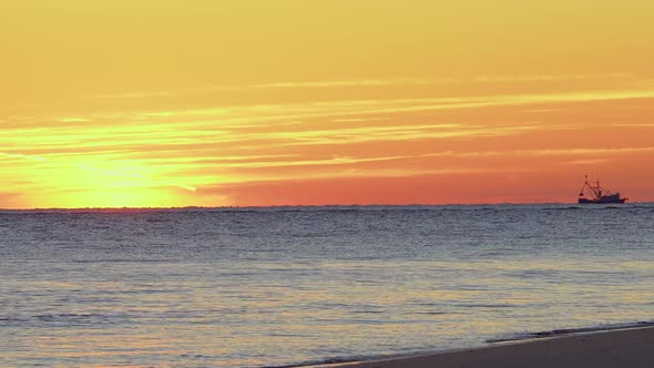 A shrimping boat sails on the horizon during sunrise at folly beach