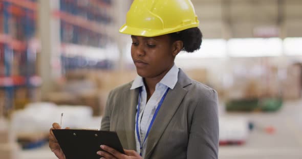 Portrait of african american female worker wearing helmet and smiling in warehouse