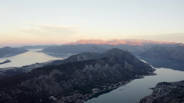 Aerial view of calm water of winding bay interrupted by huge cliffs and mountains during golden hour