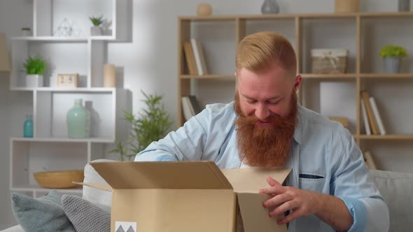 Redhead Man Sit on Couch Opens Parcel Box Feels Satisfied Looking Sincerely Glad By Delivered Goods