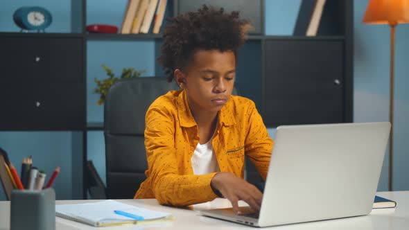 African Schoolboy Sitting at Wooden Table Tired Doing Homework at Home