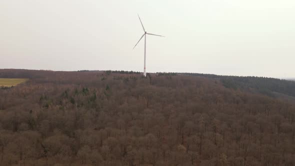 Aerial footage of approaching flight towards a fast spinning wind turbine towering on top of a brown