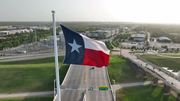 Texas Flag waves in wind. Aerial orbit reveals Trinity River and downtown Dallas TX skyline.