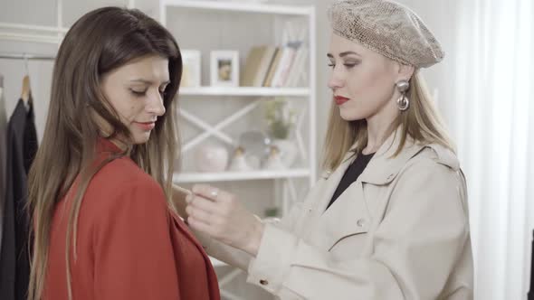 Confident Smiling Young Dressmaker Examining Jacket on Client in Atelier