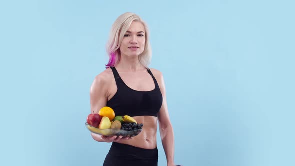 Beautiful Athletic Woman Holds a Plate of Fruit in Hand and Shows Phone with the Greenscreen App