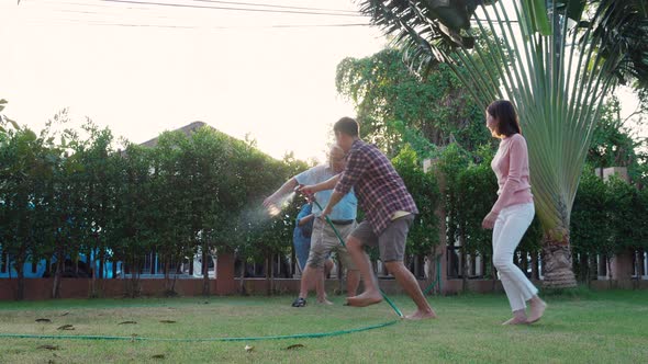 Happy Family playing together during Retired Grandfather watering the plants at the home garden.