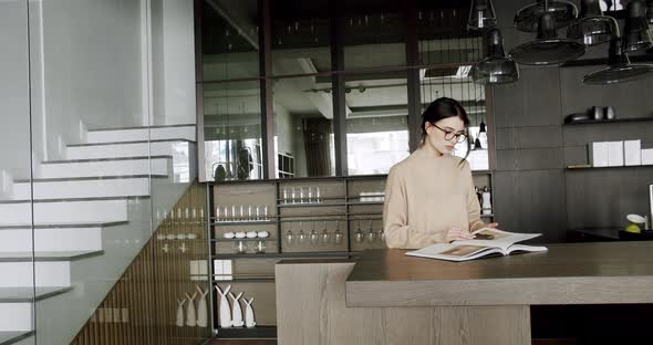 Attractive Motivated Female in Eyeglasses Enjoy in Kitchen Room and Read a Book