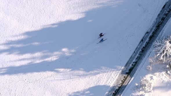 Two cross-country skiing people are walking through a snowy landscape as topshot straight from above