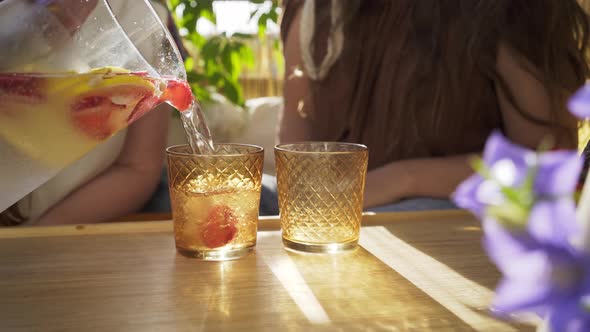 Woman Fills Glasses with Cold Lemonade on Wooden Table