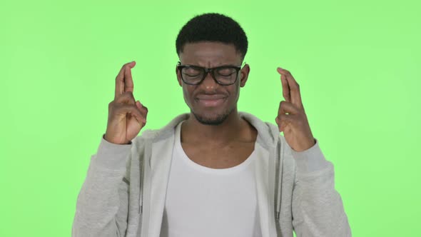 African Man Praying with Fingers Crossed on Green Background
