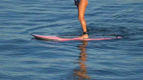 A young woman SUP surfing in a bikini on a stand-up paddleboard surfboard.