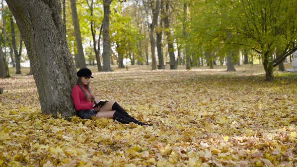 View of Young Positive Girl Writing Down Thoughts in a Notebook on a Park Lawn