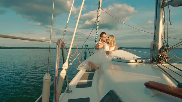 Brides Sit on a Yacht, Looking at Each Other. Beautiful Landscape Behind Them. The Bride Smiles